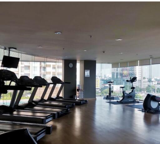 Modern gym within an apartment building with various exercise machines and a view of the city