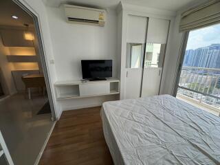 Spacious bedroom with a large bed, built-in shelving and a television, featuring hardwood floors and a city view