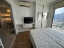 Spacious bedroom with a large bed, built-in shelving and a television, featuring hardwood floors and a city view