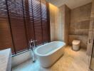 Modern bathroom with freestanding bathtub, wood blinds, and marble tiles