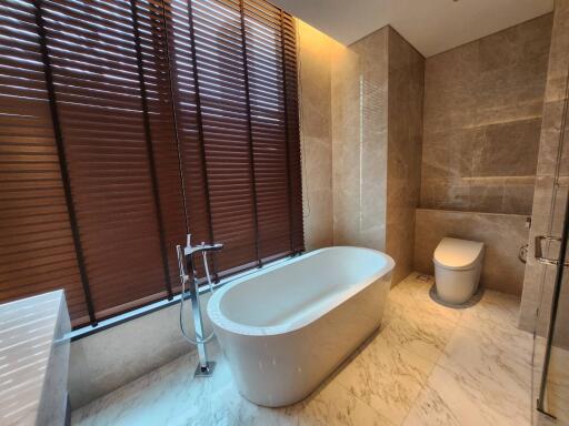 Modern bathroom with freestanding bathtub, wood blinds, and marble tiles