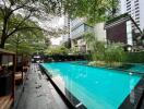 Modern outdoor swimming pool surrounded by lush greenery and city buildings