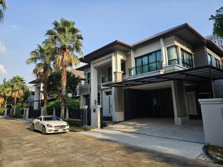 Modern two-story house with a white car parked in the driveway, surrounded by palm trees