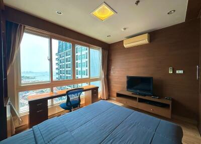 Cozy bedroom with a large window offering city views, including a comfortable bed, TV and a work desk