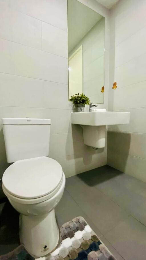 Modern white tiled bathroom with wall-mounted sink, toilet, and mirror