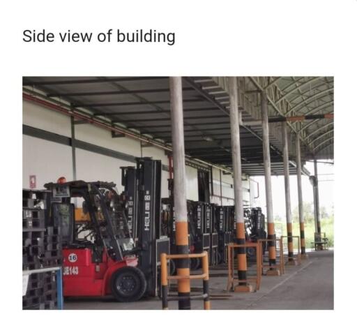 Industrial warehouse with multiple forklifts lined up under a covered area