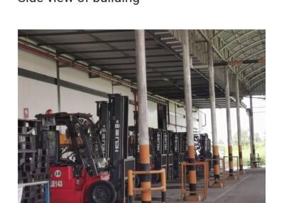 Industrial warehouse with multiple forklifts lined up under a covered area