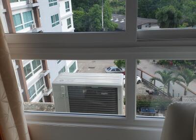 A room with a large window showing an air conditioning unit and a view of nearby buildings and greenery