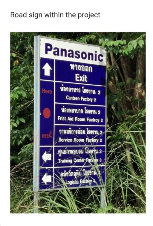 Directional signage with text in Thai script pointing to various locations within a project, surrounded by greenery