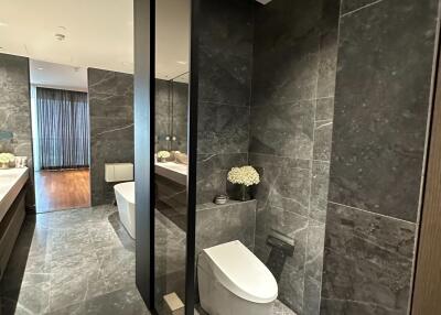 Modern bathroom with dark tiled walls and floors, featuring a white toilet, vanity, and a large mirror