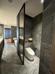 Modern bathroom with dark tiled walls and floors, featuring a white toilet, vanity, and a large mirror