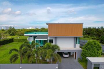Aerial view of a modern two-story house with a lush garden and clear skies