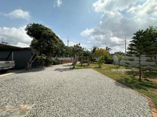 Gravel driveway leading to a home with a lush garden and clear skies