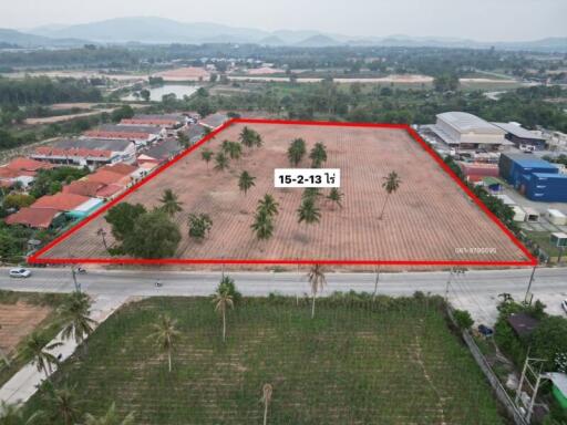 Aerial view of a vacant land plot outlined in red with palm trees and nearby residential area