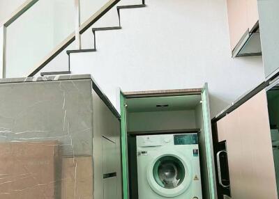 Compact laundry room with a washing machine under the stairs