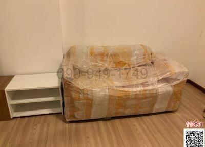 Wrapped sofa and a white shelf in a living room with hardwood flooring