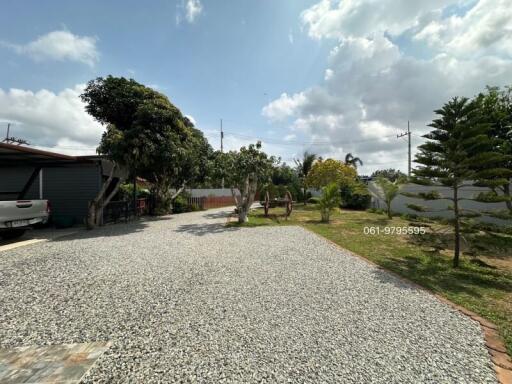 Spacious open driveway with gravel surface surrounded by greenery under a blue sky
