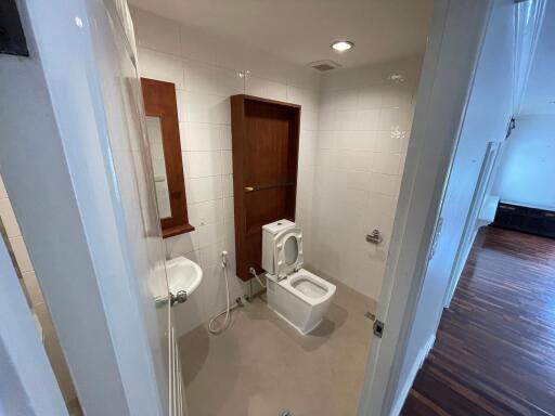 Compact bathroom with white tiles, glass shower enclosure, and wooden door