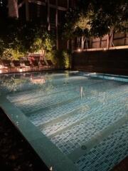 Illuminated outdoor swimming pool at night with surrounding deck chairs