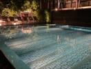 Illuminated outdoor swimming pool at night with surrounding deck chairs