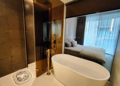 Modern bathroom with freestanding tub and glass partition overlooking bedroom