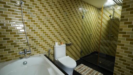 Modern bathroom with golden tile walls, a bathtub, and a glass shower