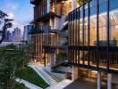 Modern multi-story building facade at twilight with illuminated interiors and lush greenery