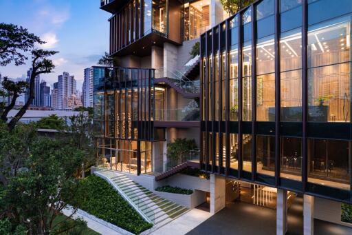 Modern multi-story building facade at twilight with illuminated interiors and lush greenery