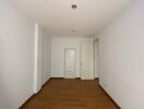 Bright and empty corridor with wooden flooring leading to rooms with white doors