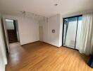 Spacious empty room with hardwood flooring, large windows and a glass door leading to an outdoor area