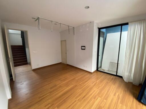 Spacious empty room with hardwood flooring, large windows and a glass door leading to an outdoor area