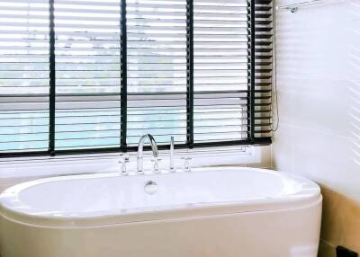 Spacious bathroom with a large bathtub and modern fixtures near a window with blinds