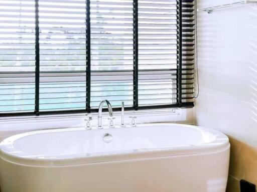 Spacious bathroom with a large bathtub and modern fixtures near a window with blinds