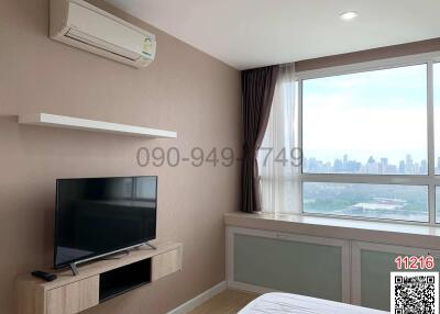 Modern bedroom with city view, including a bed, television, and air conditioning unit