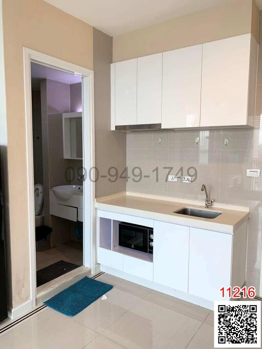 Modern kitchen with white cabinets, stainless steel sink, and built-in appliances, leading to a bathroom