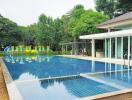 Elegant residential outdoor swimming pool with adjacent pool house amidst lush greenery