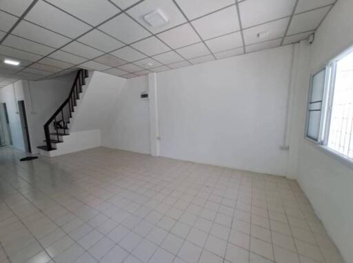 Spacious empty room with tiled flooring, large windows, and staircase