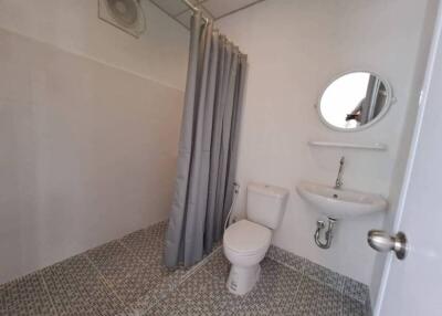 Compact bathroom with tiled floor, white toilet, pedestal sink, mirror, and shower curtain