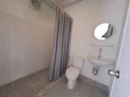 Compact bathroom with tiled floor, white toilet, pedestal sink, mirror, and shower curtain