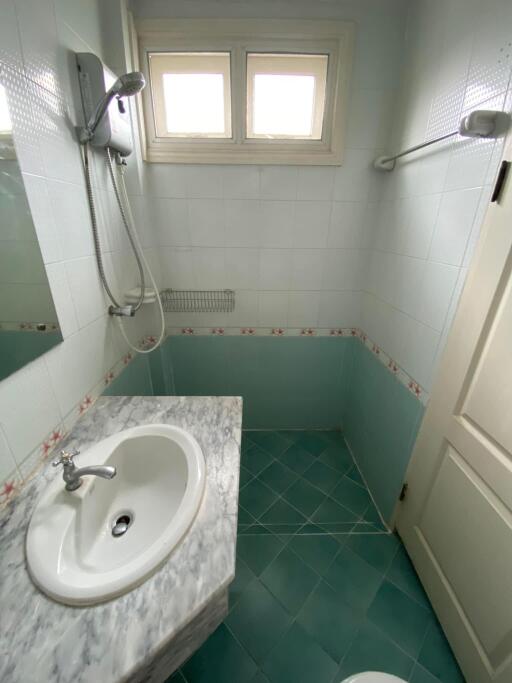 Compact bathroom with corner shower, sink, and teal tiles