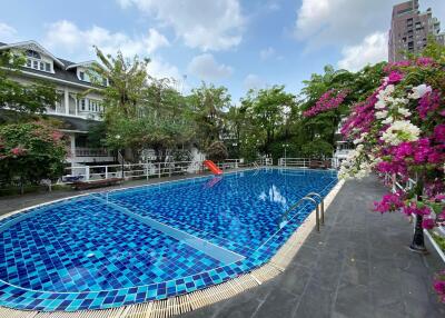 Residential outdoor swimming pool surrounded by flowers with buildings in the background