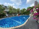 Residential outdoor swimming pool surrounded by flowers with buildings in the background