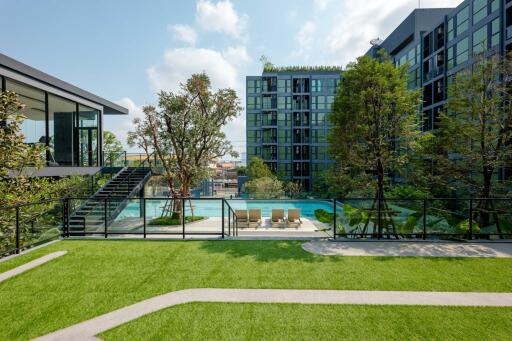 Luxurious outdoor area with a swimming pool, lush greenery, and modern building in the background