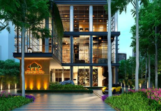 Modern multi-story building exterior at dusk with illuminated interiors, landscaping, and a luxury car parked outside