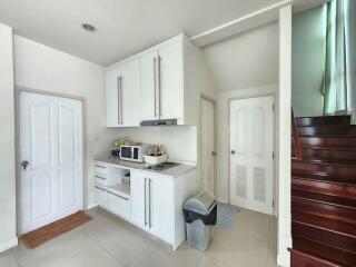 Compact modern kitchen with white cabinetry and wooden staircase