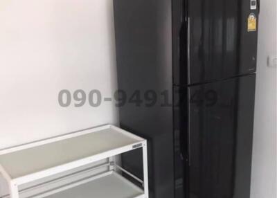 Compact kitchen with large black refrigerator and metal shelving unit