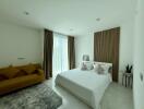 Modern bedroom interior with a comfortable double bed, stylish sofa, and large window with curtains