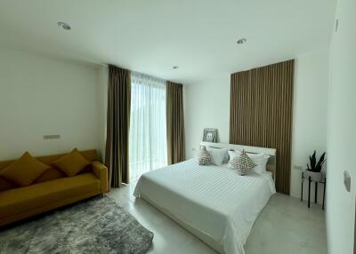 Modern bedroom interior with a comfortable double bed, stylish sofa, and large window with curtains
