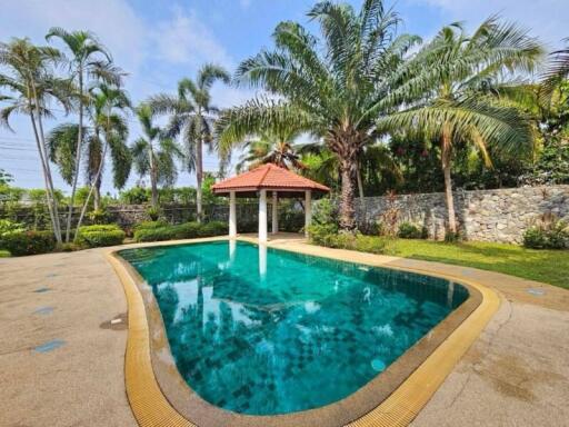 Elegant outdoor swimming pool with a shaded gazebo, surrounded by lush palms and tropical landscaping