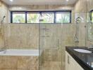 Modern bathroom with natural stone tiles, glass shower, and bathtub